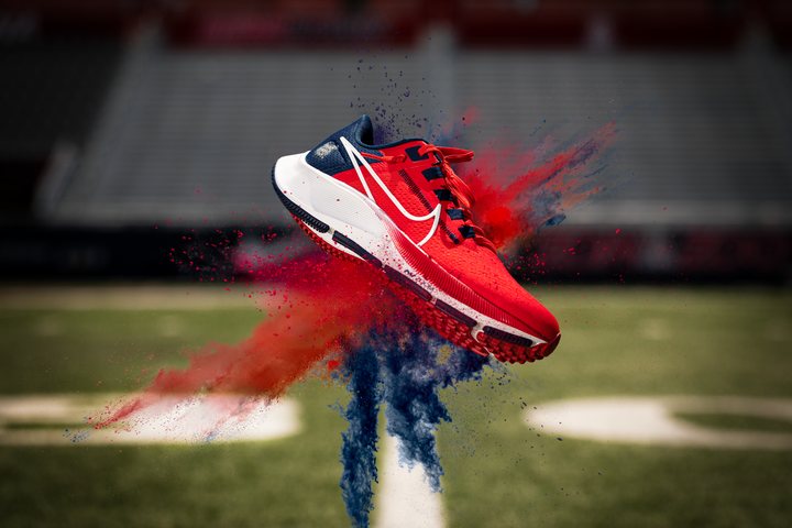 Running shoe suspended in a burst of red and blue powder above a field
